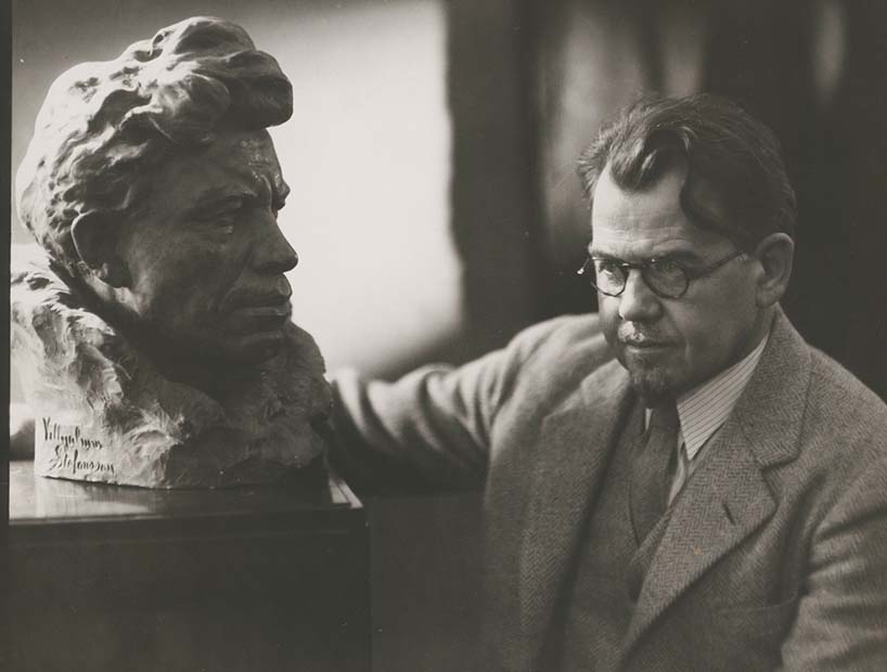 A man sitting with a bust sculpture.