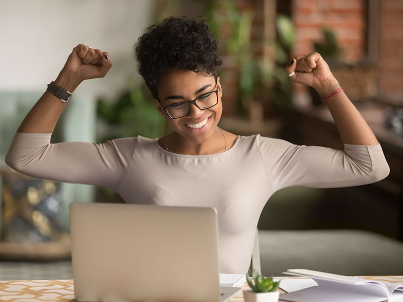 Black student rejoicing with fists in the air in front of a laptop.