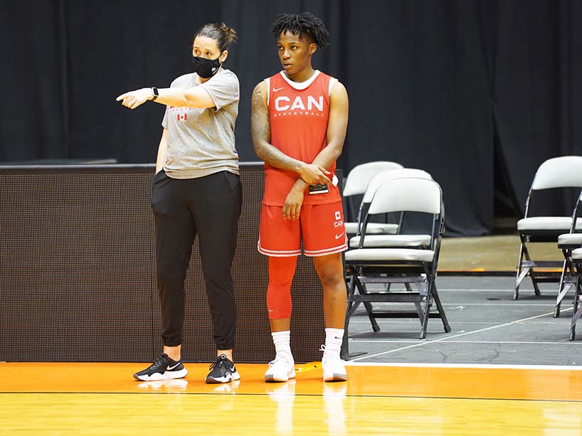 A coach and a basketball player stand on the court together.