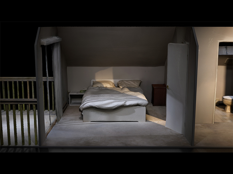 Photo of a bed in a grey room surrounded by walls on either side.