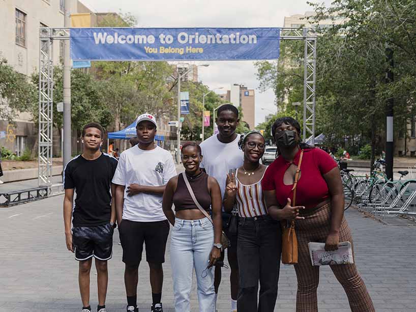 Campus street with six students and a ‘welcome to orientation’ banner.