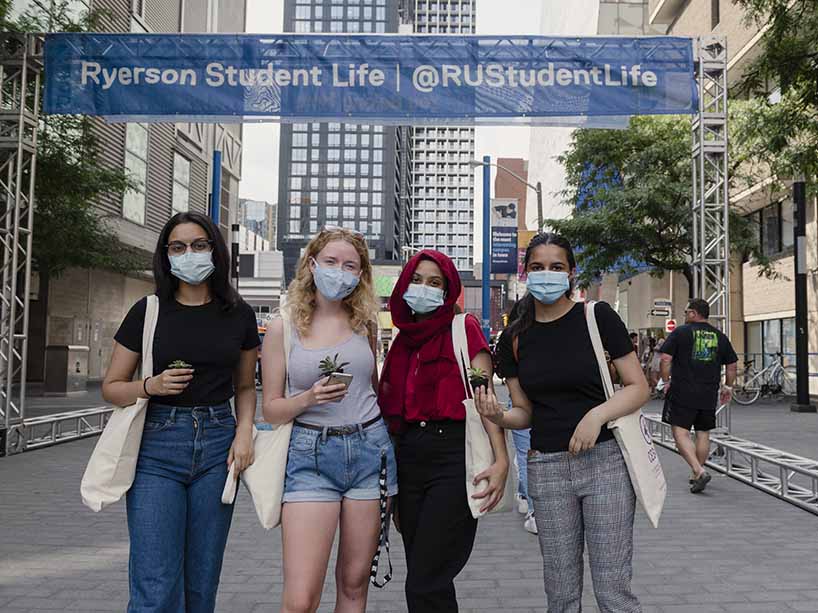 Four students holding potted plants and wearing masks in front of a Ryerson Student Life banner.