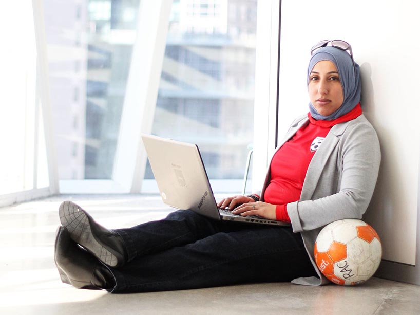 Shireen Ahmed sits in a windowsill with her laptop, soccer ball at her side, looking at the camera