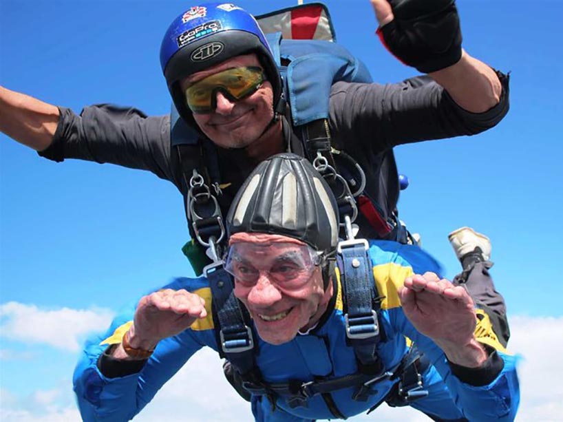 An elderly man in the sky during a tandem skydive, harnessed to an instructor.