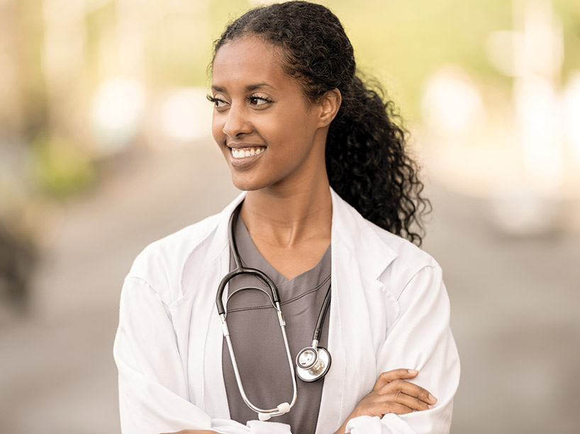A female doctor stands outside with her arms crossed.