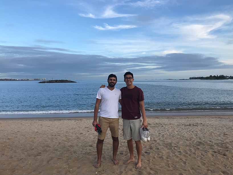 Two male students standing on a beach together. 