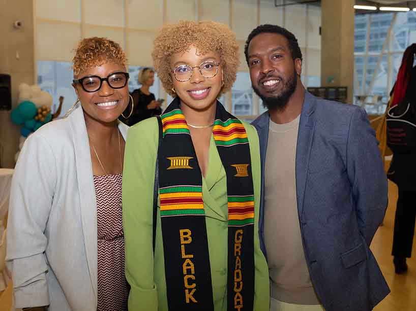 Nya Martin-Hemming wearing a kente stole at the graduation ceremony standing in between her parents.