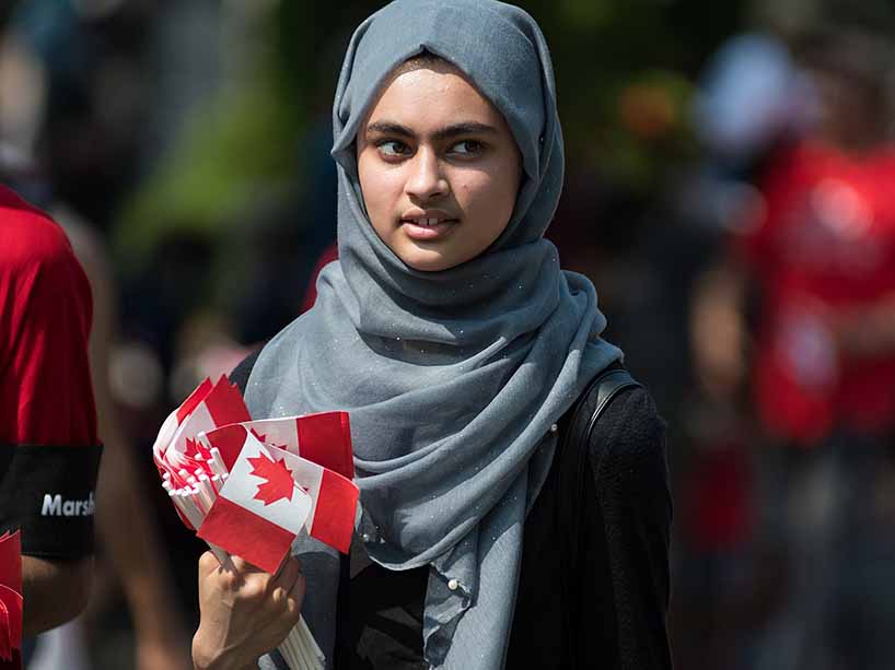 Young woman in a hijab holds a handful of small Canadian flags