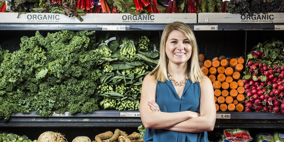 Smiling woman standing in front of fully stocked produce shelves with arms crossed