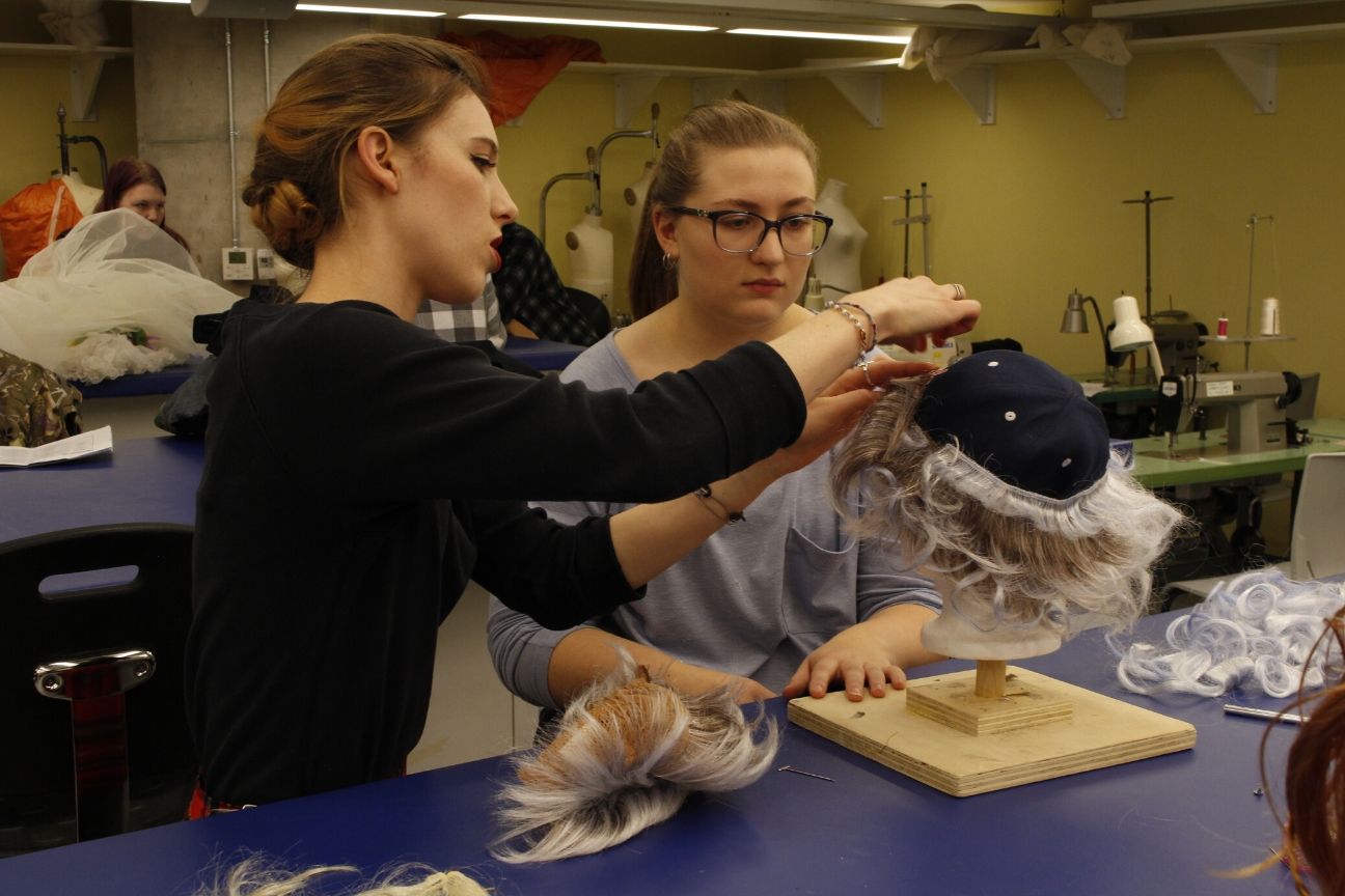 An instructors shows a student how to make a wig off of a ball cap