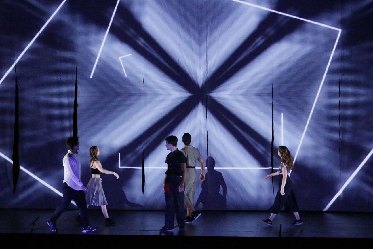 4 actors walking on stage, looking at the geometric projections behind them.
