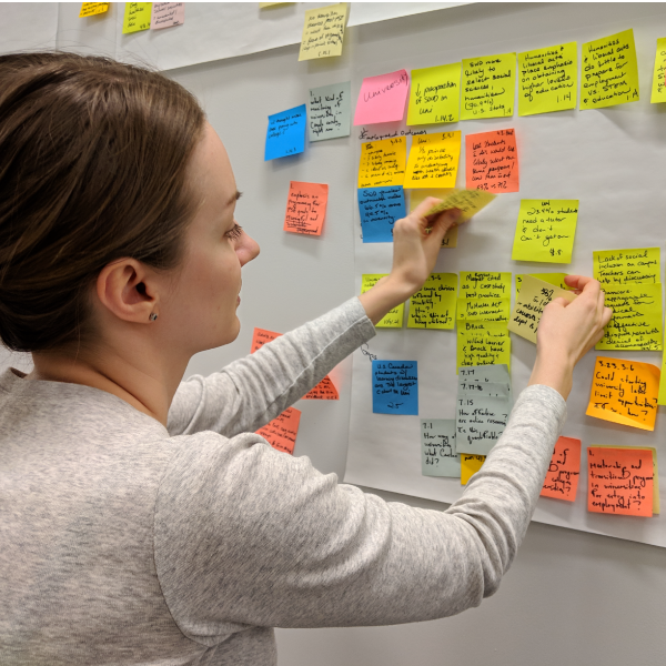 Student meticulously places a sticky note onto a collection of colourful stickies on the wall