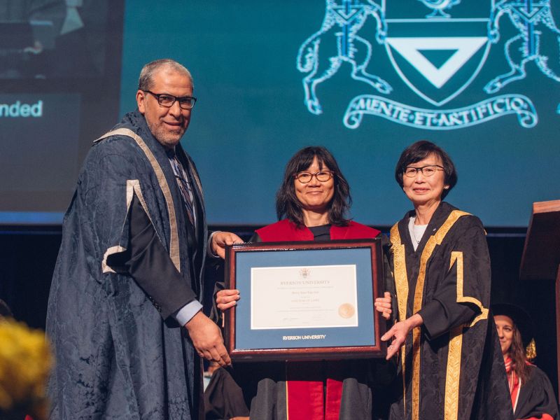 President Lachemi and Chancellor Janice Fukakusa C.M. present a framed honorary doctorate to Justice Avvy Yao-Yao Go on the stage at convocation