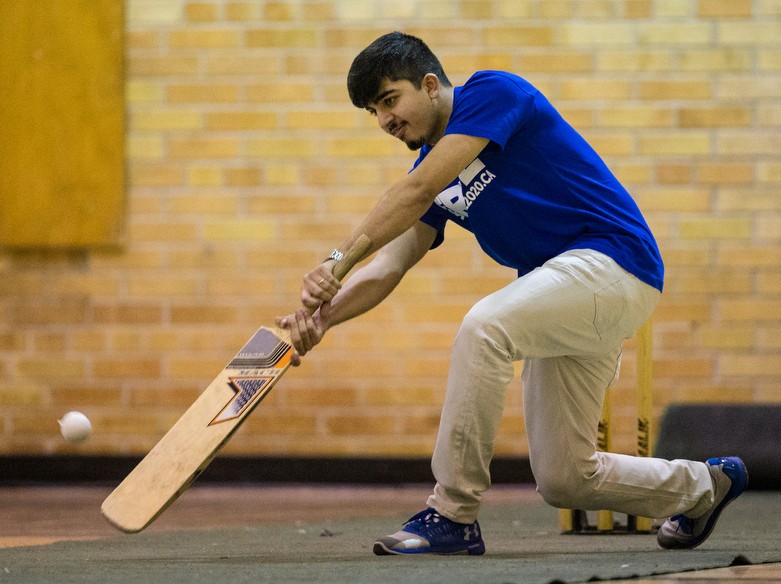 A cricket player holding a bat in a kneeling position and is about to hit approaching ball.