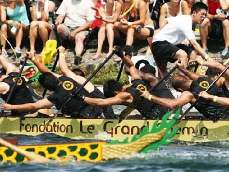 Dragon boat team paddles in a race while spectators watch in the background.