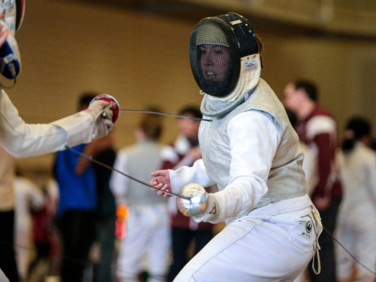A girl in her fencing gear during a match. A crowd is behind her.