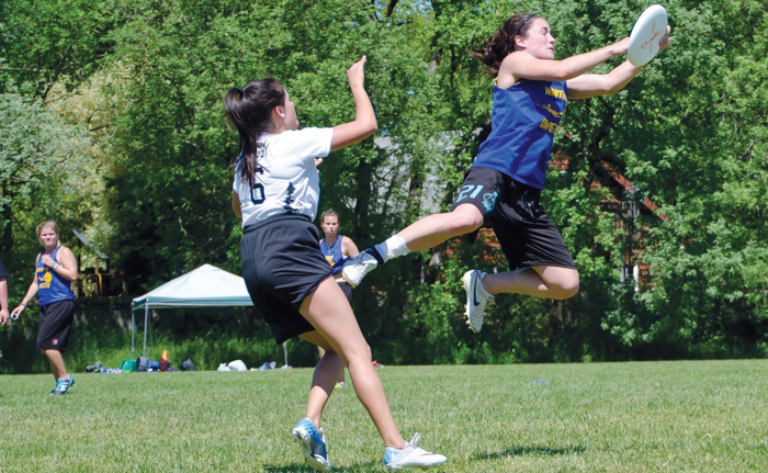 A male ultimate frisbee player is mid-play on the field. The frisbee is in the air.