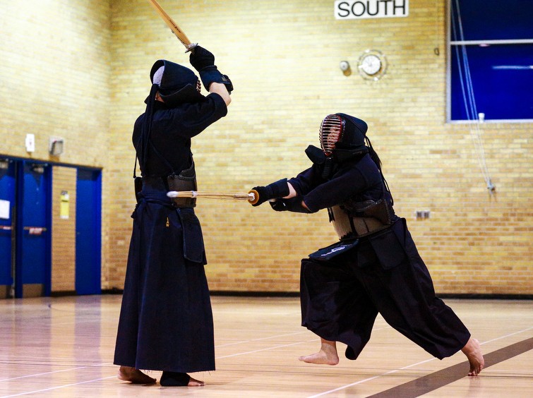 A class practices Kendo at Ryerson. All participants are in a line holding bamboo swords.