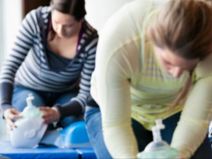 Two females performing CPR on manikins during a first aid kit class.