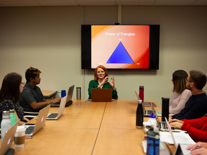 Professor Candace Monson speaks to a group around a boardroom table