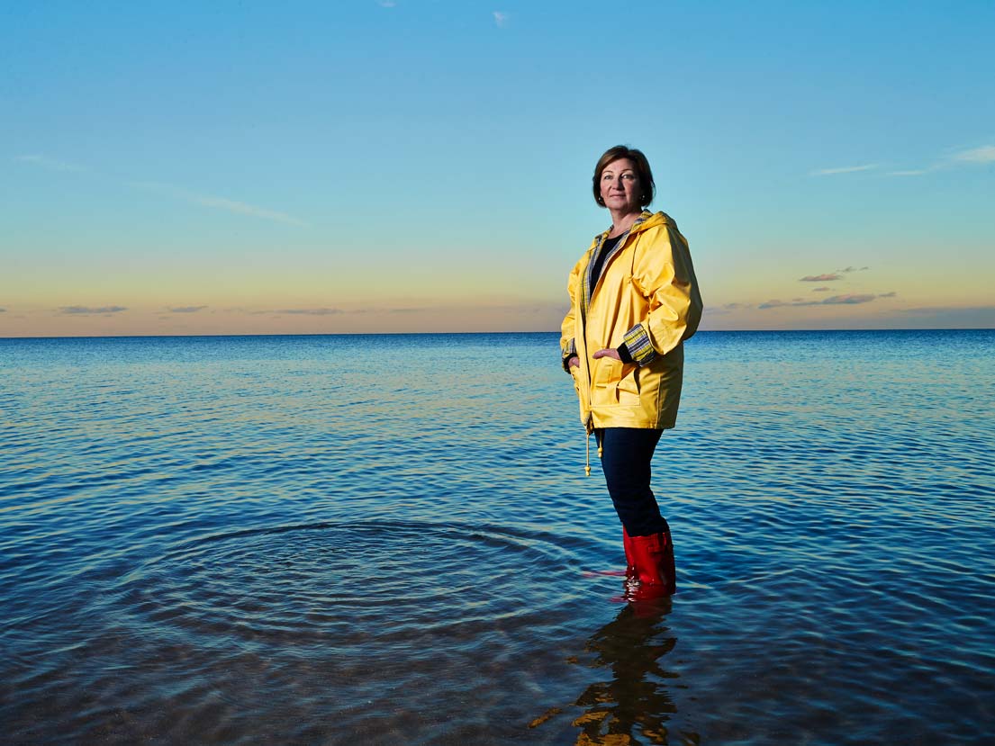 Professor Carolyn Johns stands alone in Lake Ontario in ankle-deep water at sunset.