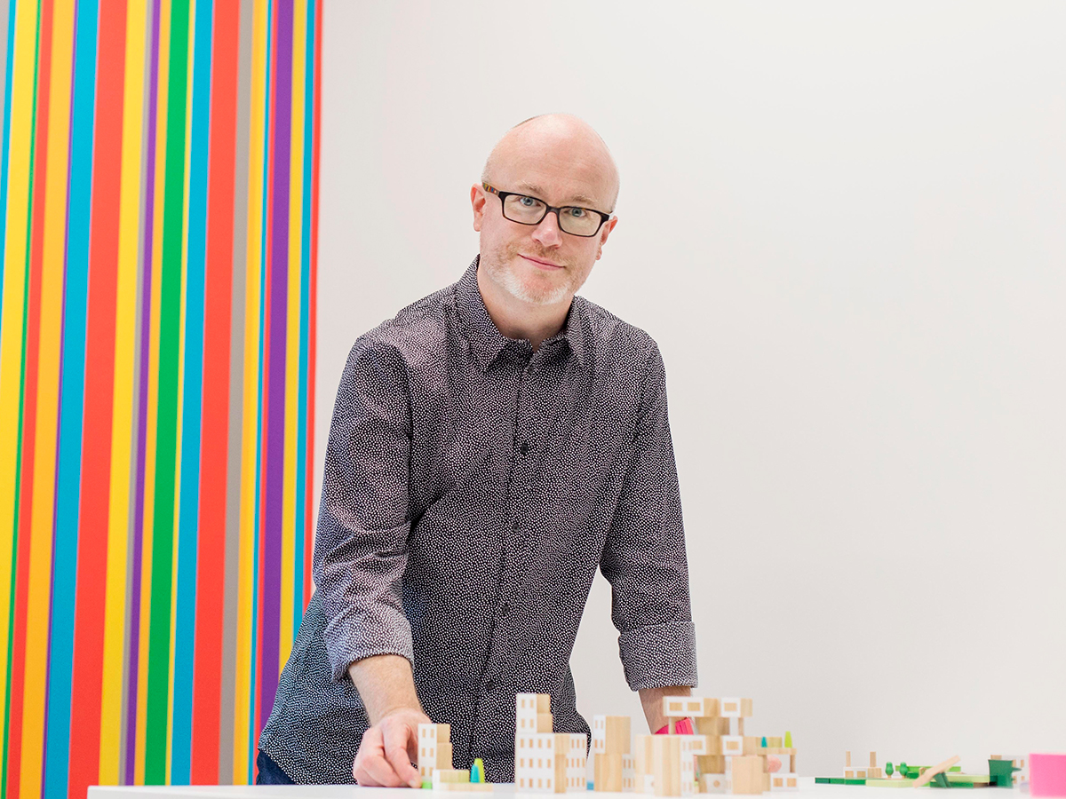 Professor David Gauntlett stands in front of a diorama of a city built out of small wooden blocks