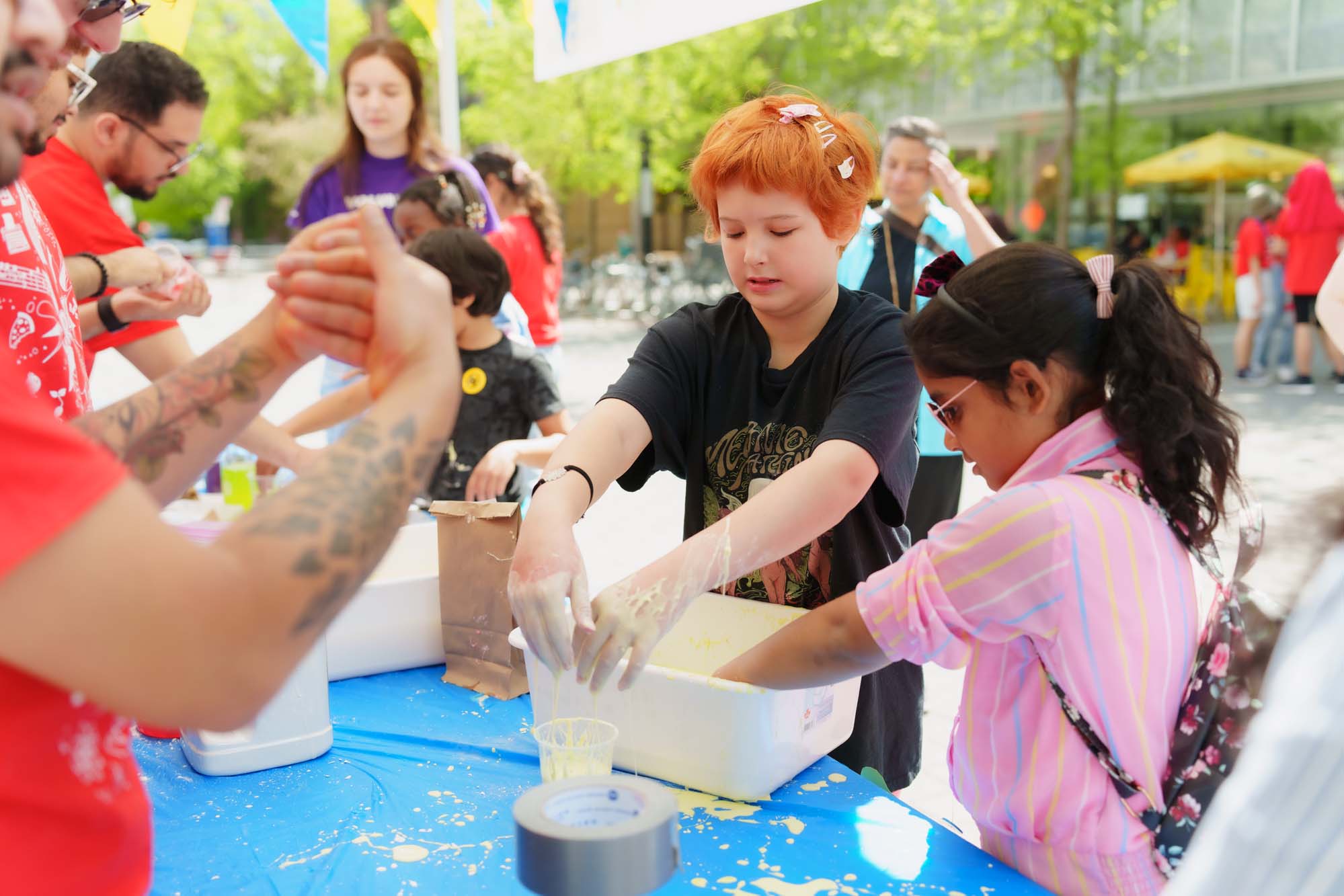 Two children playing with yellow slime with their hands in a white container.