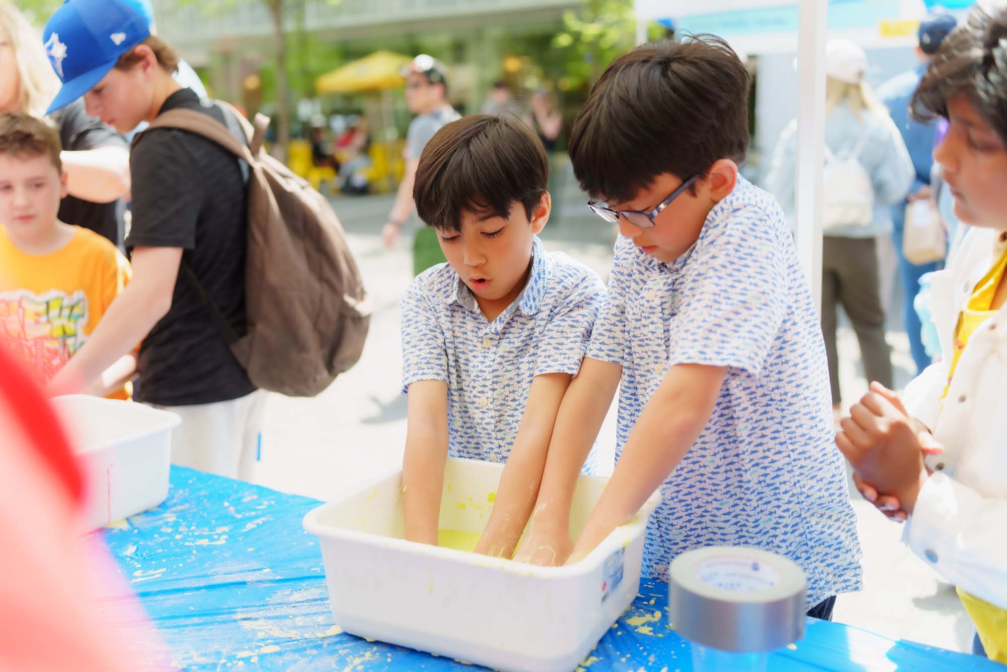 Two kids playing with the yellow slime in a white container at the booth.