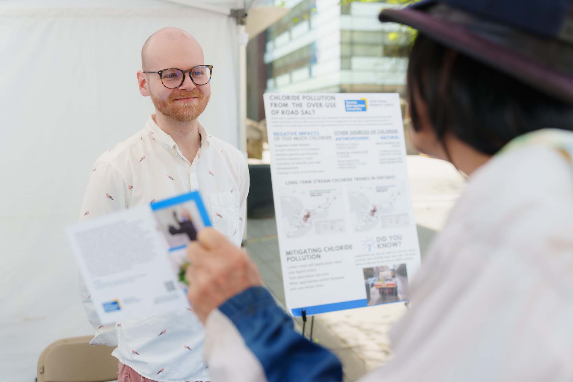 A volunteer standing next to a presentation board about chloride pollution from the over-use of road salt is listening to a participant at the TMU Urban Water booth. 