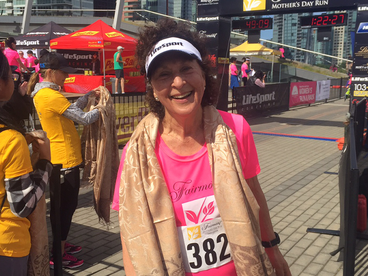 Dr. Melanie Panitch, standing at the end of a race, wearing a pink t-shirt and white hat, smiling. 