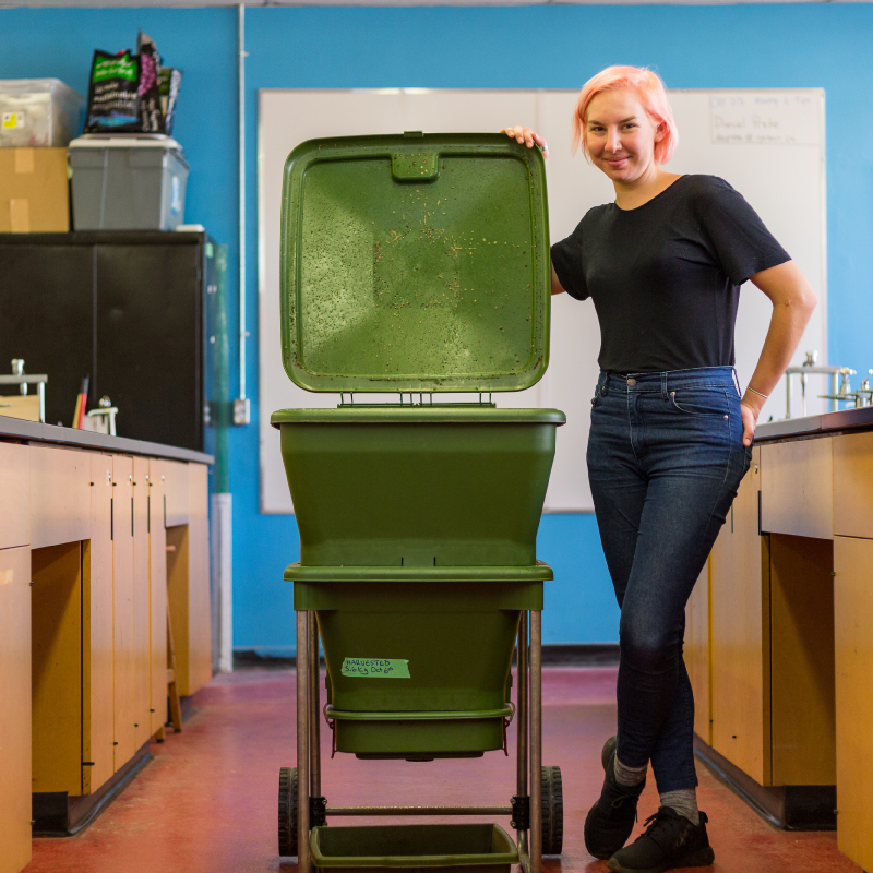 woman smiling with a large compost bin