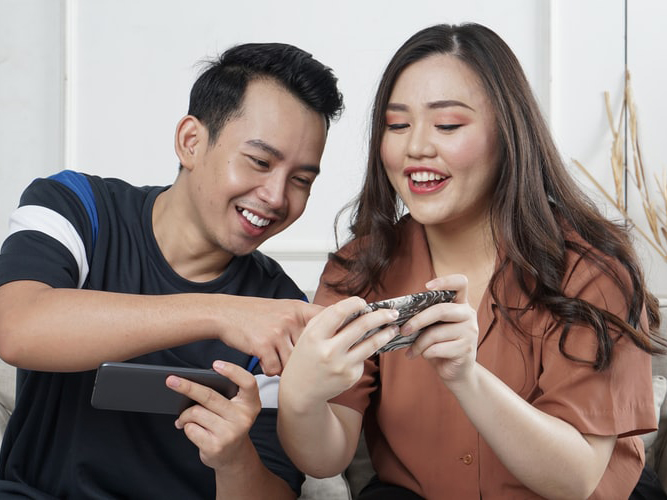 Two people side by side holding their phones and laughing.