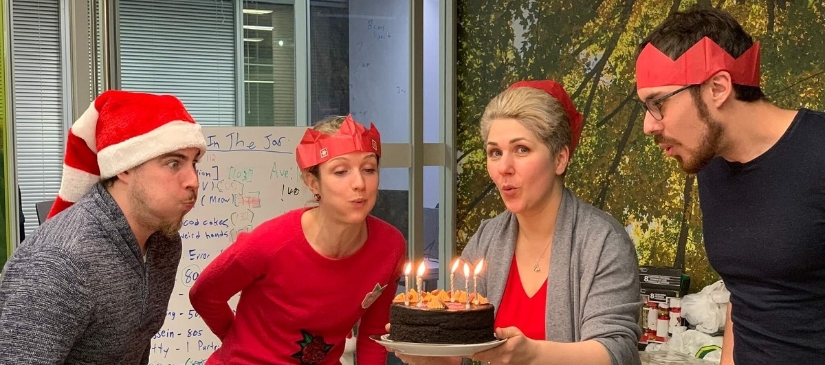 Four CRL members blowing out candles on a cake with various hats and paper crowns on their heads.