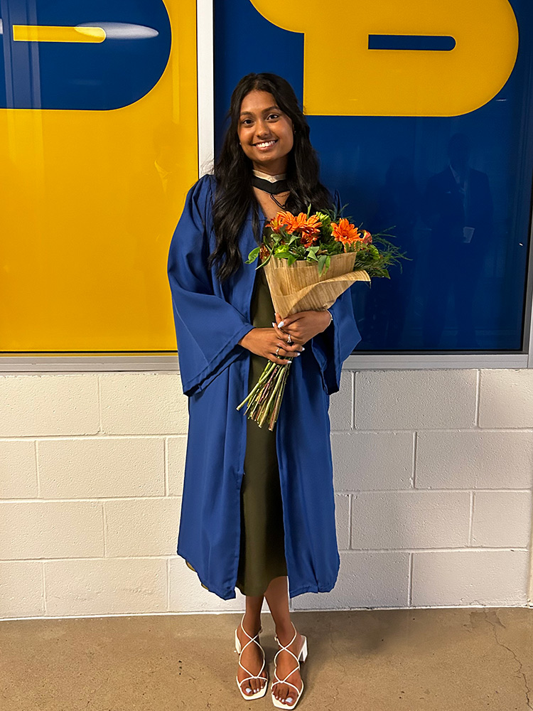 Megan Florian wearing her convocation grown and holding flowers at the Mattamy Athletic Centre 