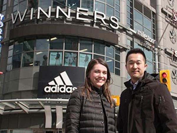 A young man and woman standing in the middle of the Yonge and dundas intersection in front of the Adidas store on the corner