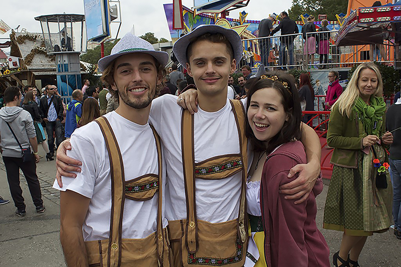 Student standing in street festival with two locals in brown overalls and hats