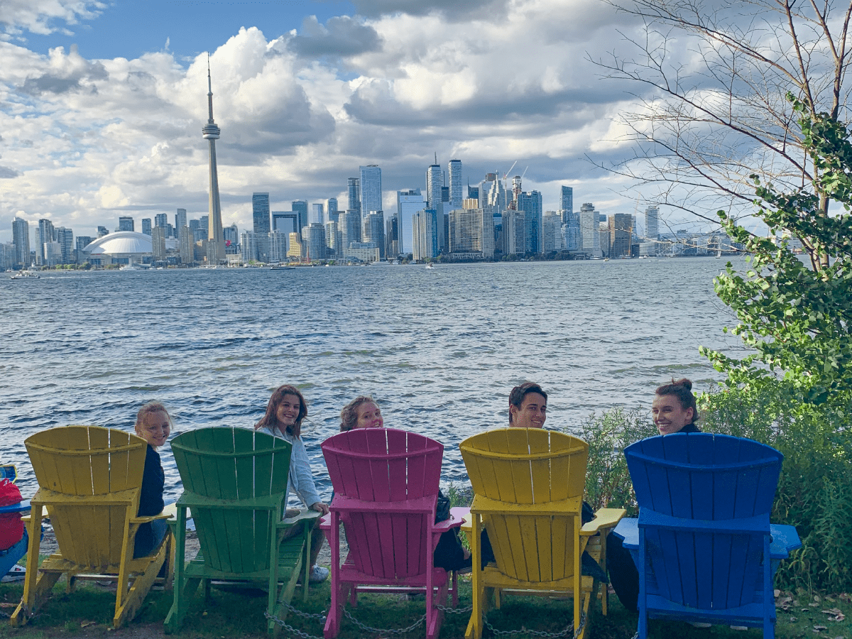 5 smiling students in colourful patio chairs by the lakeside