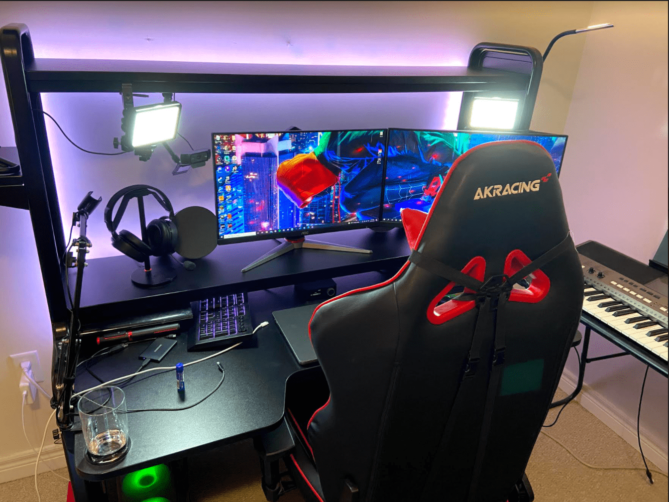 Photograph shows Dimuccio’s gaming and editing set-up in his home office. Two computer monitors sit on his black desk, along with lights, headphones, and a microphone. He has a gaming office chair.