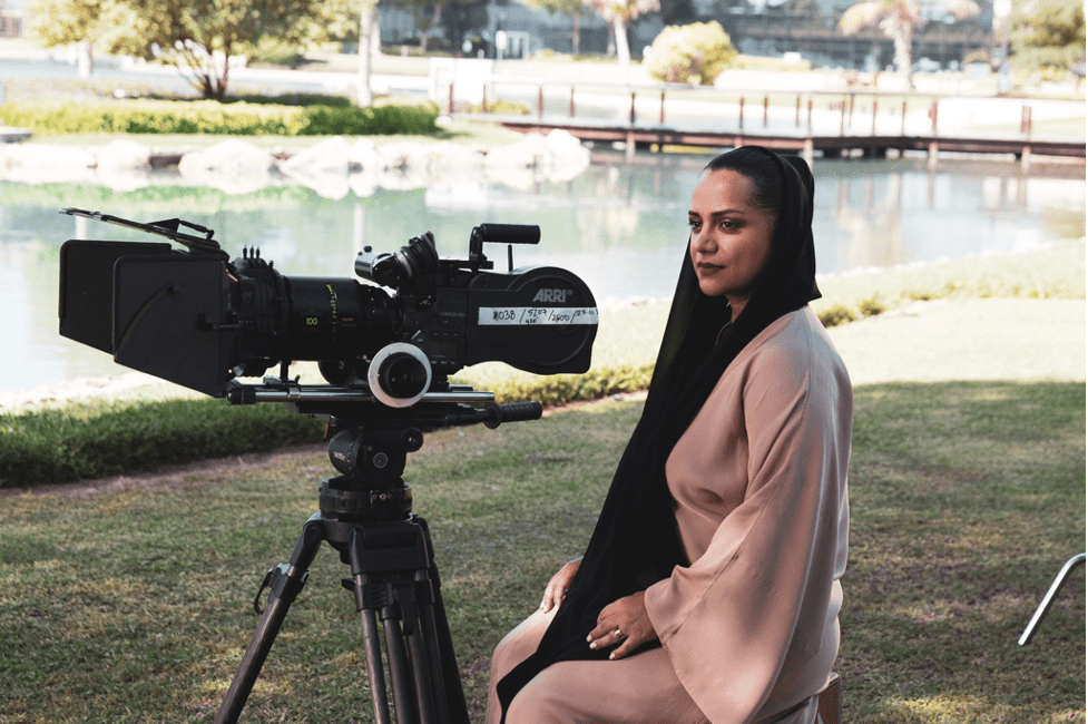 Nayla Al Khaja on set sitting on the grass looking over one of the video cameras. 