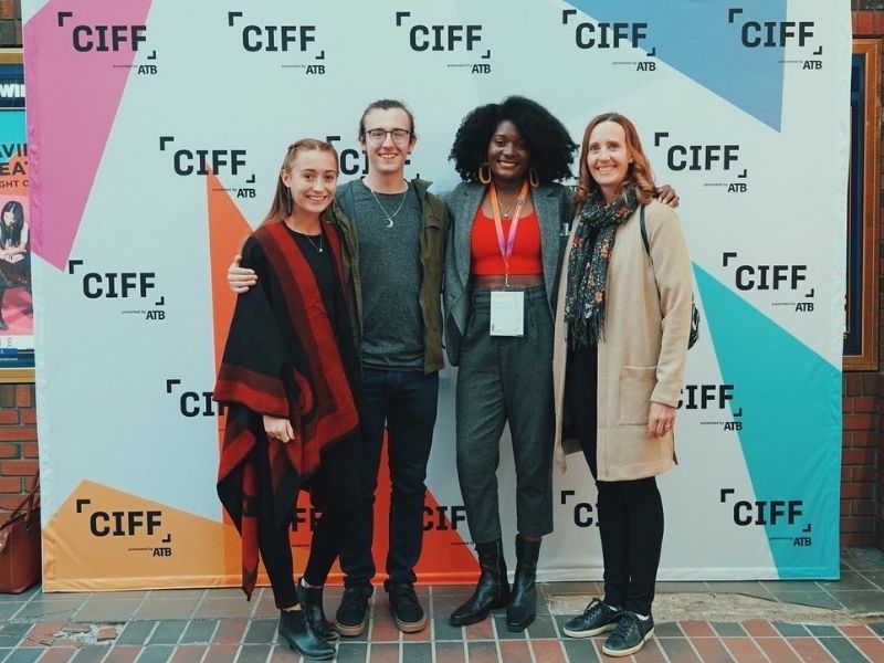Yasmine poses with friends at the CIFF in front of a colourful step-and-repeat