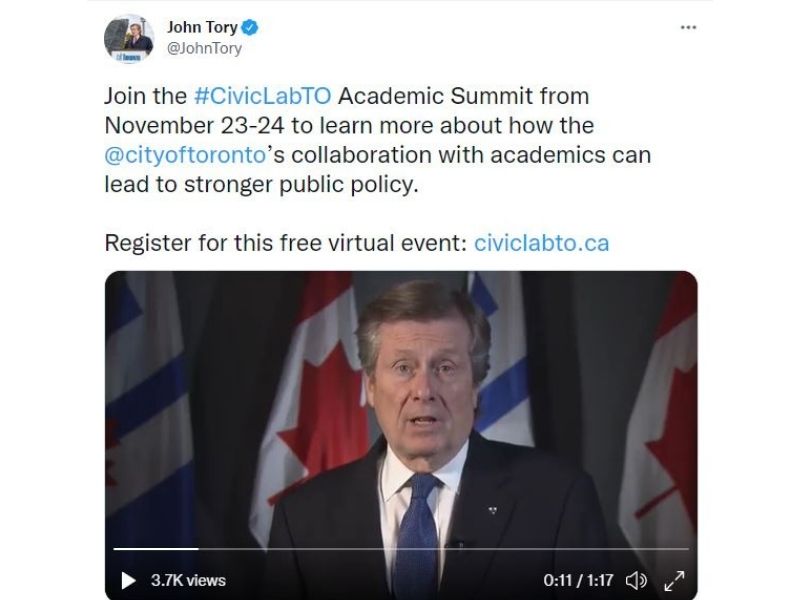 Mayor John Tory appears in a video, dressed ina  suit and tie in front of Canadian flags