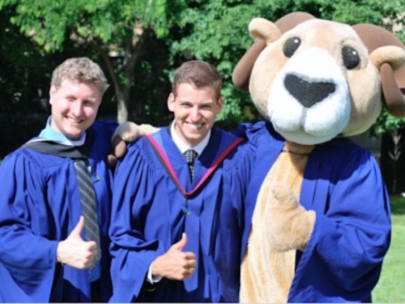 Corey Peck and Derek Rider in graduation garb posing with their thumbs up next to Ryerson Mascot Eggy