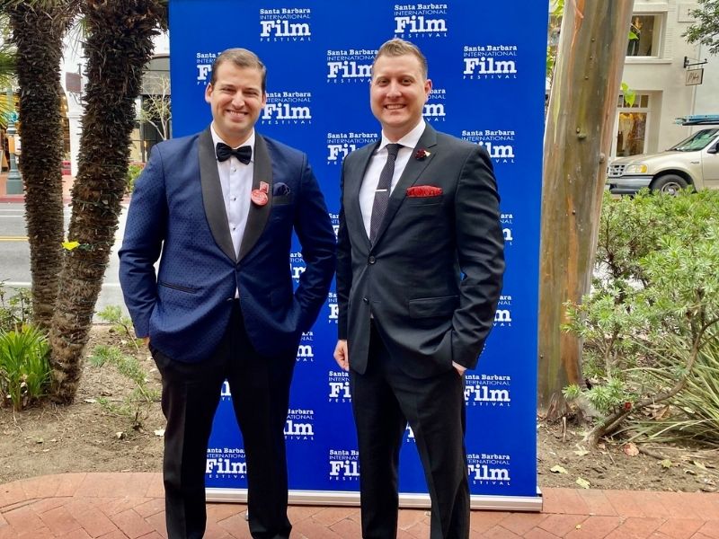 Rider and Peck stand in front of a step and repeat promoting the Santa Barbara International Film Festival dressed in suits