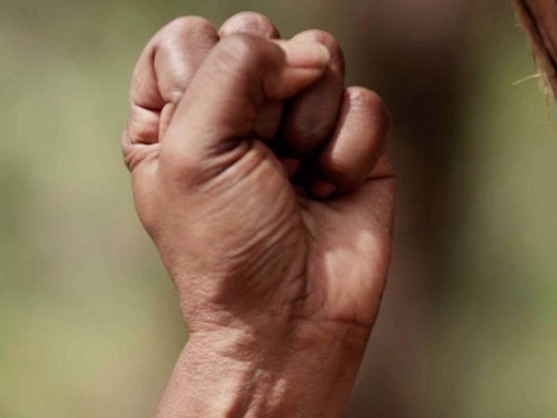 A close up of a Black person's clenched fist with a blurred background