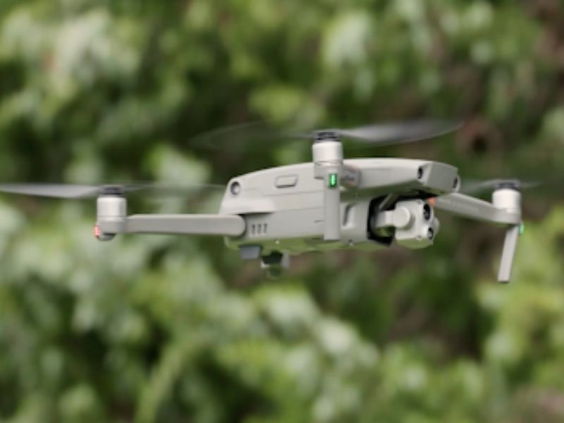 A closeup of a grey drone midflight with a blurred nature background