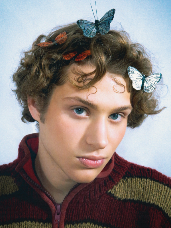 A portrait of a fashion student gazing into the camera with butterflies in his hair