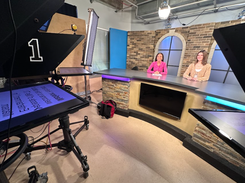 Two newscasters filming a live news production in a studio.