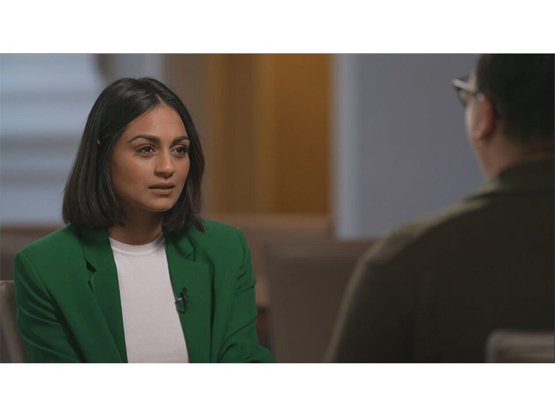 Kaul is seated opposite the woman she is interviewing. She wears a green blazer and white top, with a small microphone attached. 