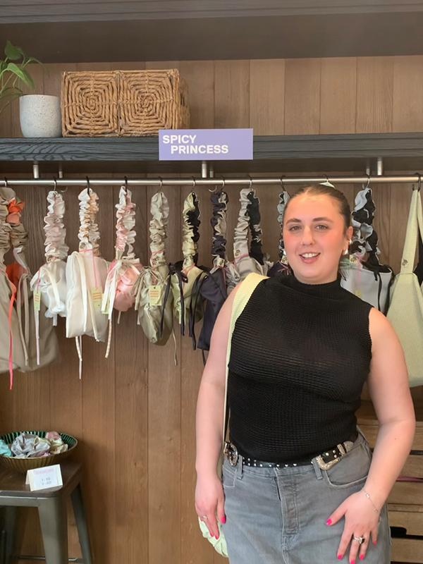Student Eva Licata is standing in front of a retail display showcasing items from her brand. 