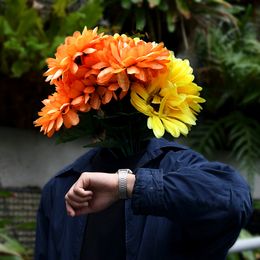 A headless man checking out his watch ( has orange and yellow flowers as his head)